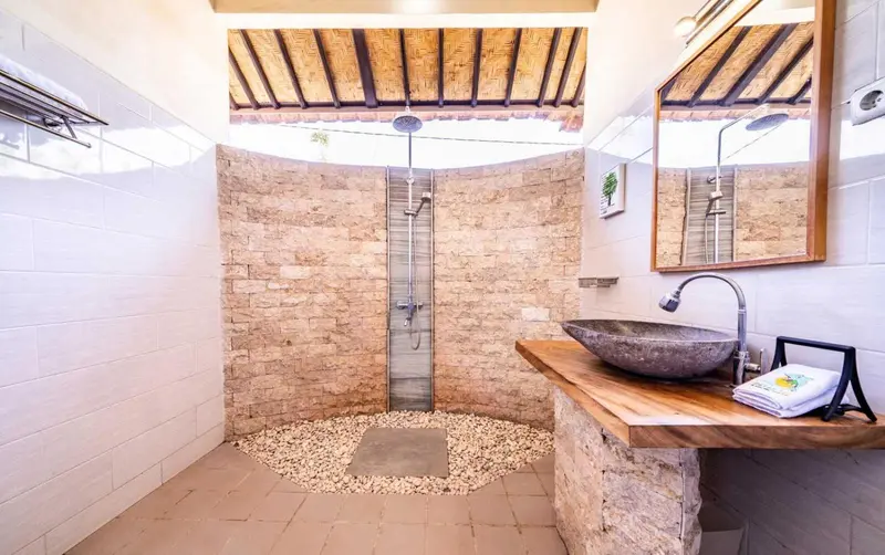 Salle de bain ouverte avec douche à l'italienne et vasque en pierre.