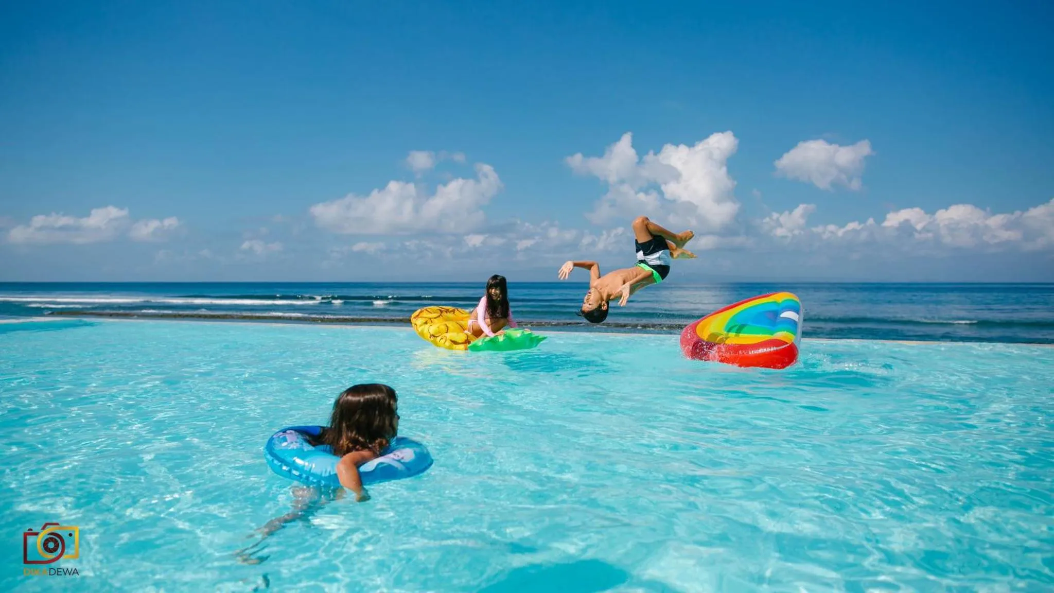 Des personnes s'amusent dans une piscine à débordement avec vue sur la mer.