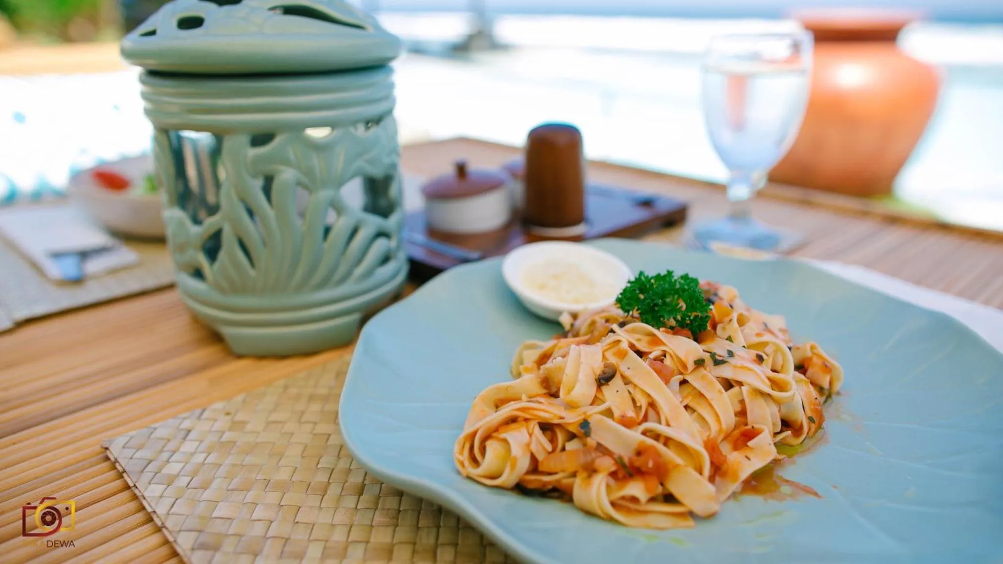 Assiette de pâtes servie sur une table en bois près de la mer.