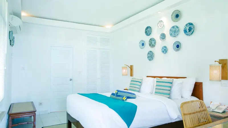 Une chambre lumineuse avec un grand lit recouvert de textiles clairs et turquoise.