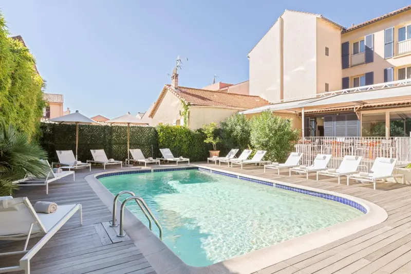 Transats blancs disposés autour d'une piscine rectangulaire ensoleillée.