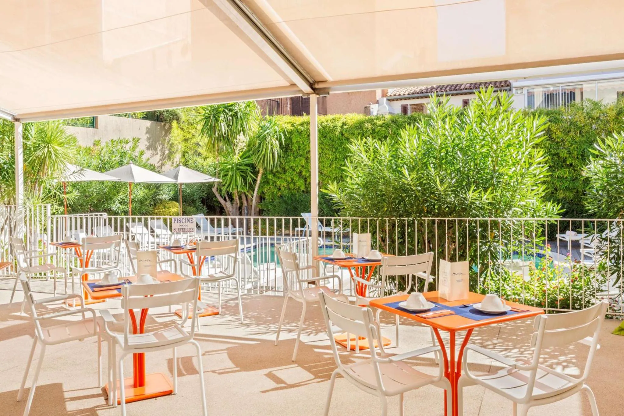 Terrasse ombragée avec tables et chaises oranges et blanches près d'une piscine.