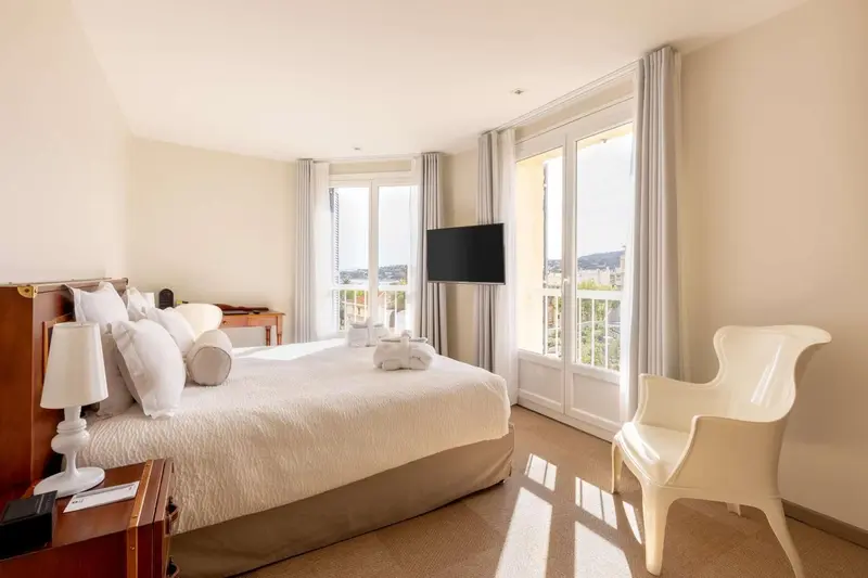 Une chambre lumineuse avec un grand lit et un accès à un balcon.