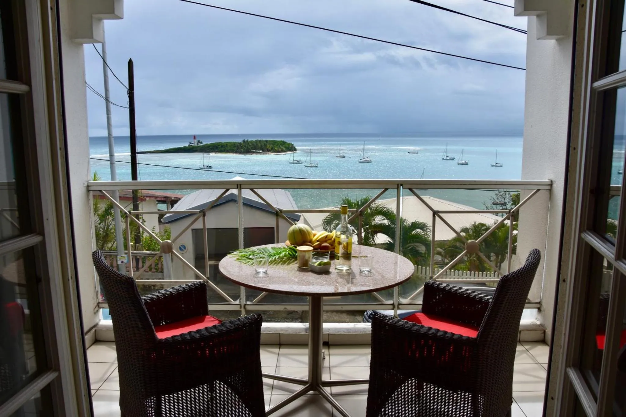Une table ronde avec des fruits et des boissons est mise en scène sur une terrasse avec vue sur la mer.