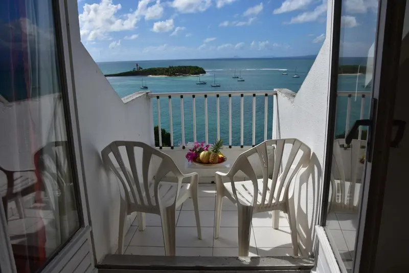 Une terrasse ensoleillée offre une vue sur la mer et une île verdoyante.