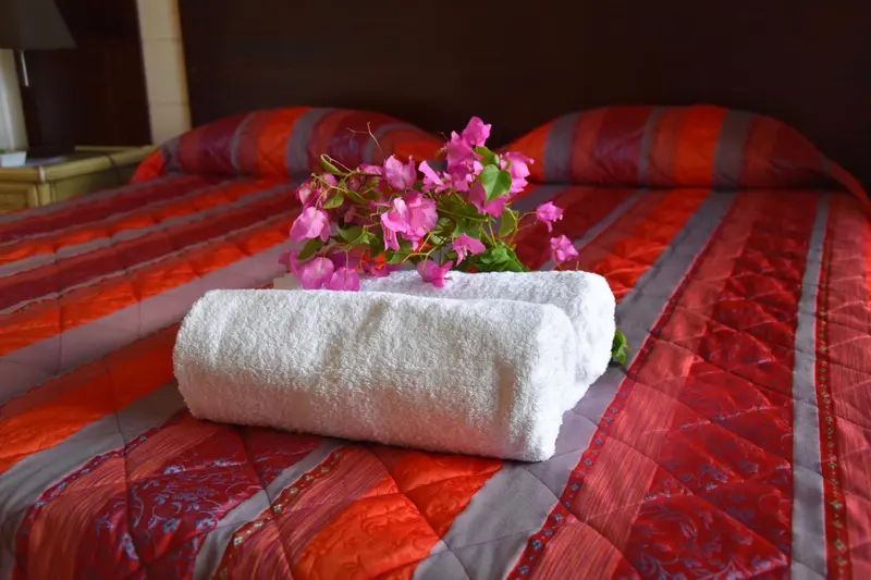 Un lit recouvert d'une courtepointe orange et de coussins décorés, agrémenté de serviettes blanches et de fleurs roses.