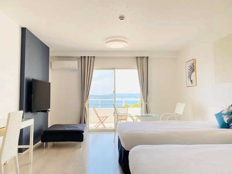 Une chambre lumineuse avec un lit et un coin salon donnant sur une vue mer.