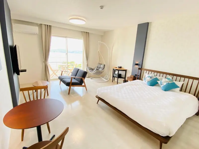 Une chambre lumineuse avec un lit et un coin salon donnant sur une vue extérieure.