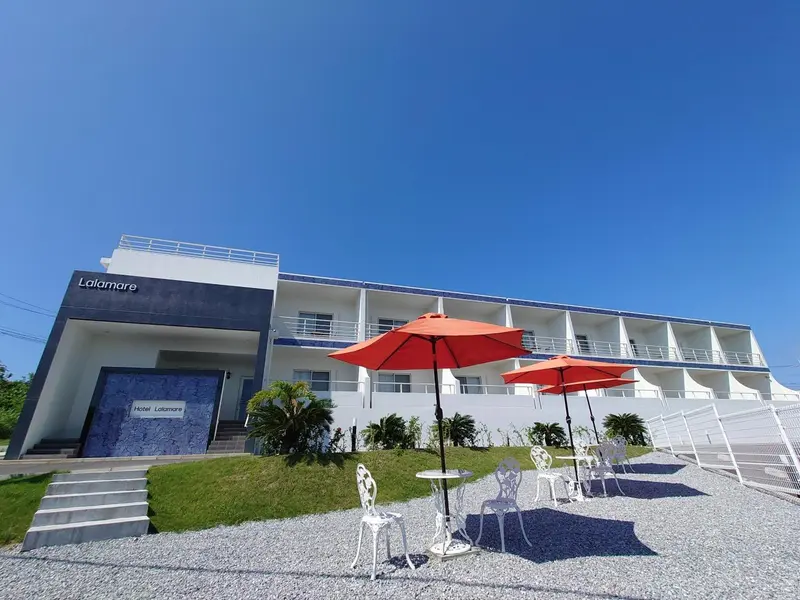 Façade blanche d'un bâtiment avec des parasols rouges et des meubles de jardin.