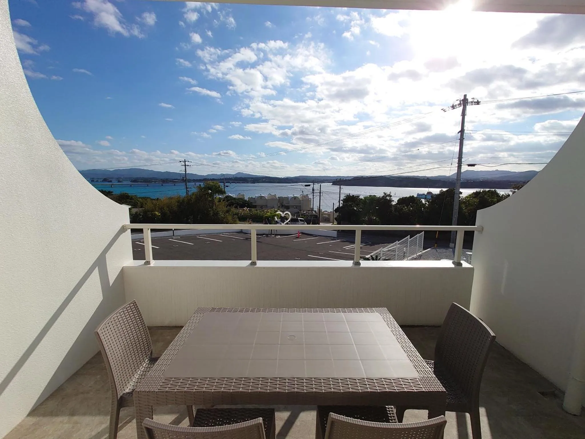 Une terrasse avec une table et des chaises offre une vue sur la mer et la végétation.