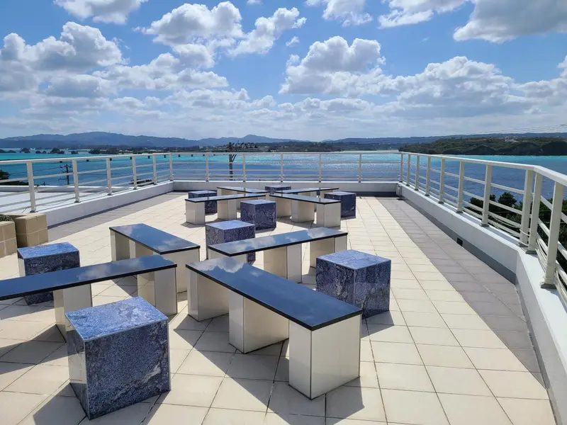 Terrasse aménagée avec tables et assises en pierre bleue sous un ciel nuageux.