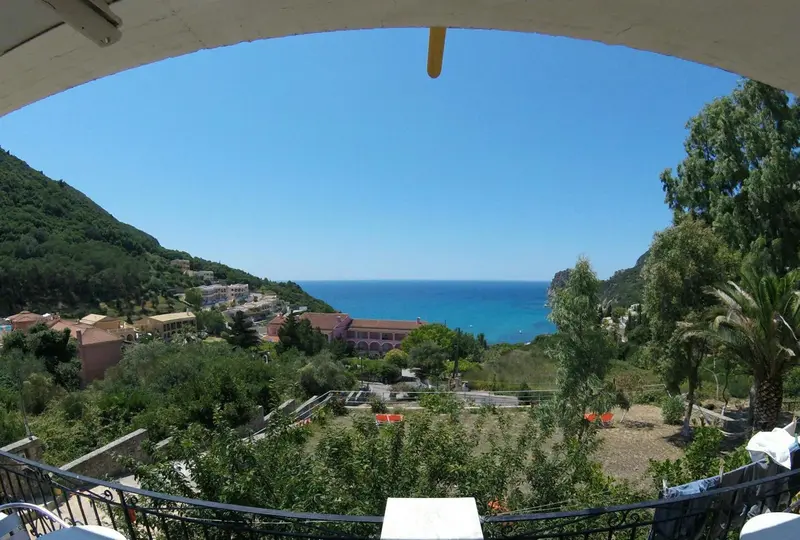 Vue d'un paysage côtier verdoyant depuis une terrasse ombragée.