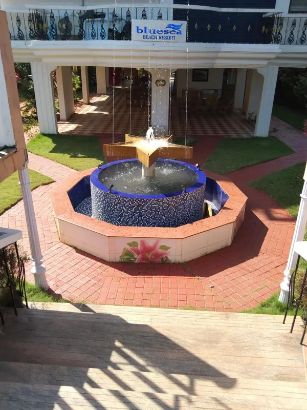 Une fontaine orne une cour pavée devant un bâtiment à colonnes.