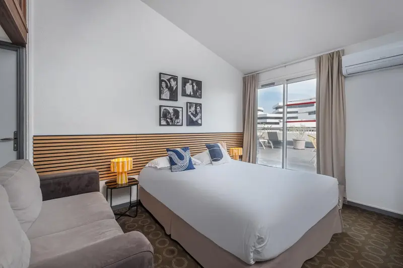 Une chambre lumineuse avec un lit double et un canapé face à une baie vitrée.