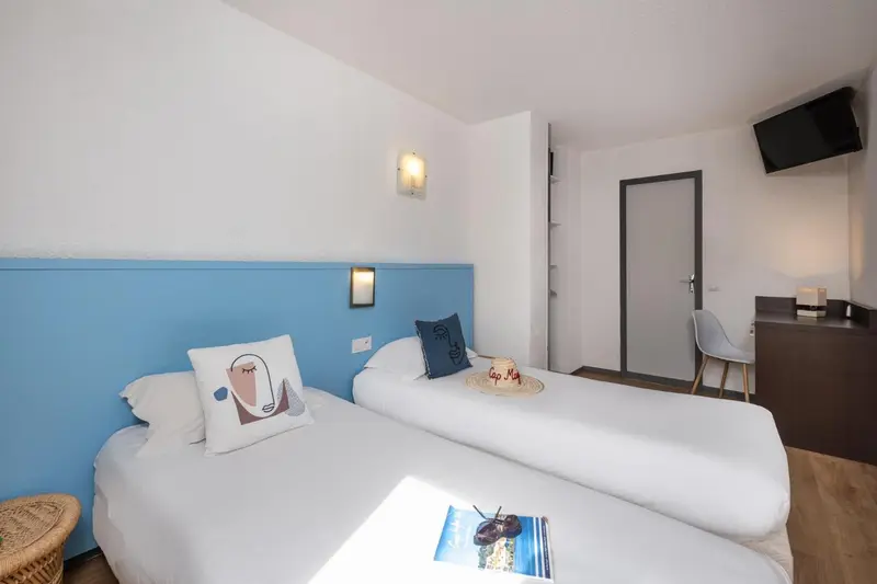 Une chambre lumineuse avec deux lits simples et un mur bleu décoré.