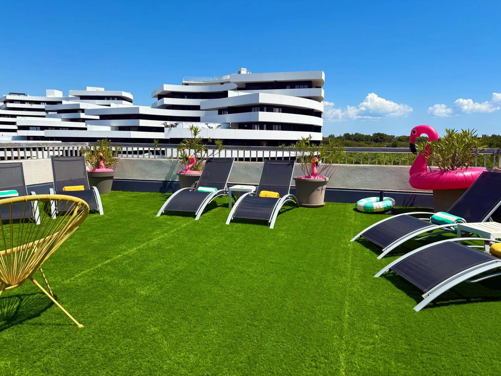 Terrasse aménagée avec des transats et une pelouse synthétique devant un bâtiment moderne.