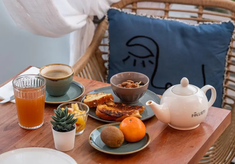 Une table en osier présente un petit-déjeuner avec une tasse de café, un jus d'orange et des fruits frais.