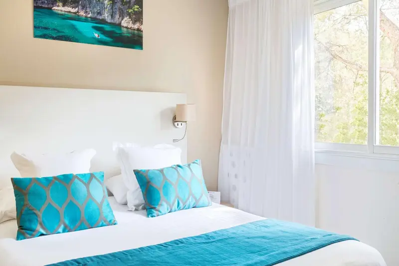Une chambre lumineuse avec un grand lit recouvert d'une courtepointe turquoise et de coussins décoratifs.