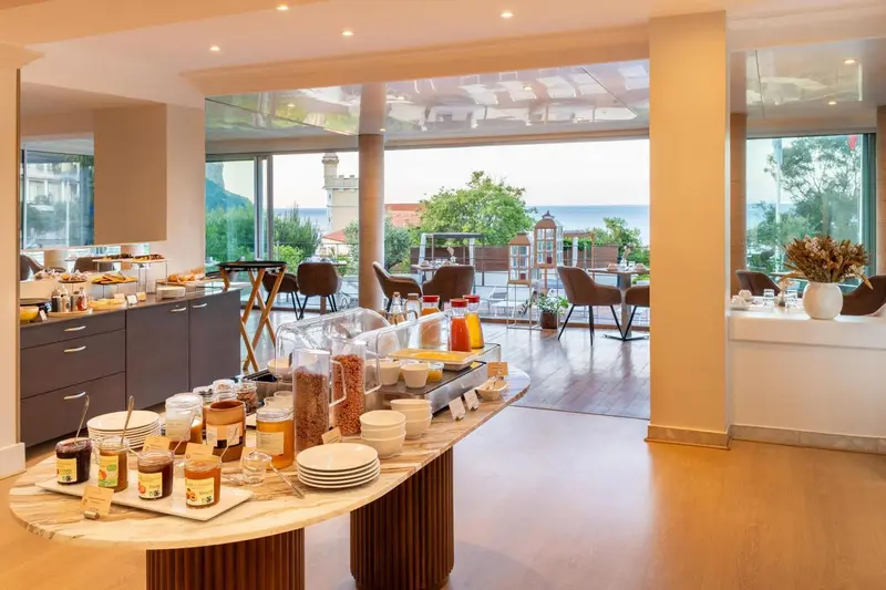 Un buffet propose des céréales, des confitures et des pâtisseries dans une salle lumineuse.