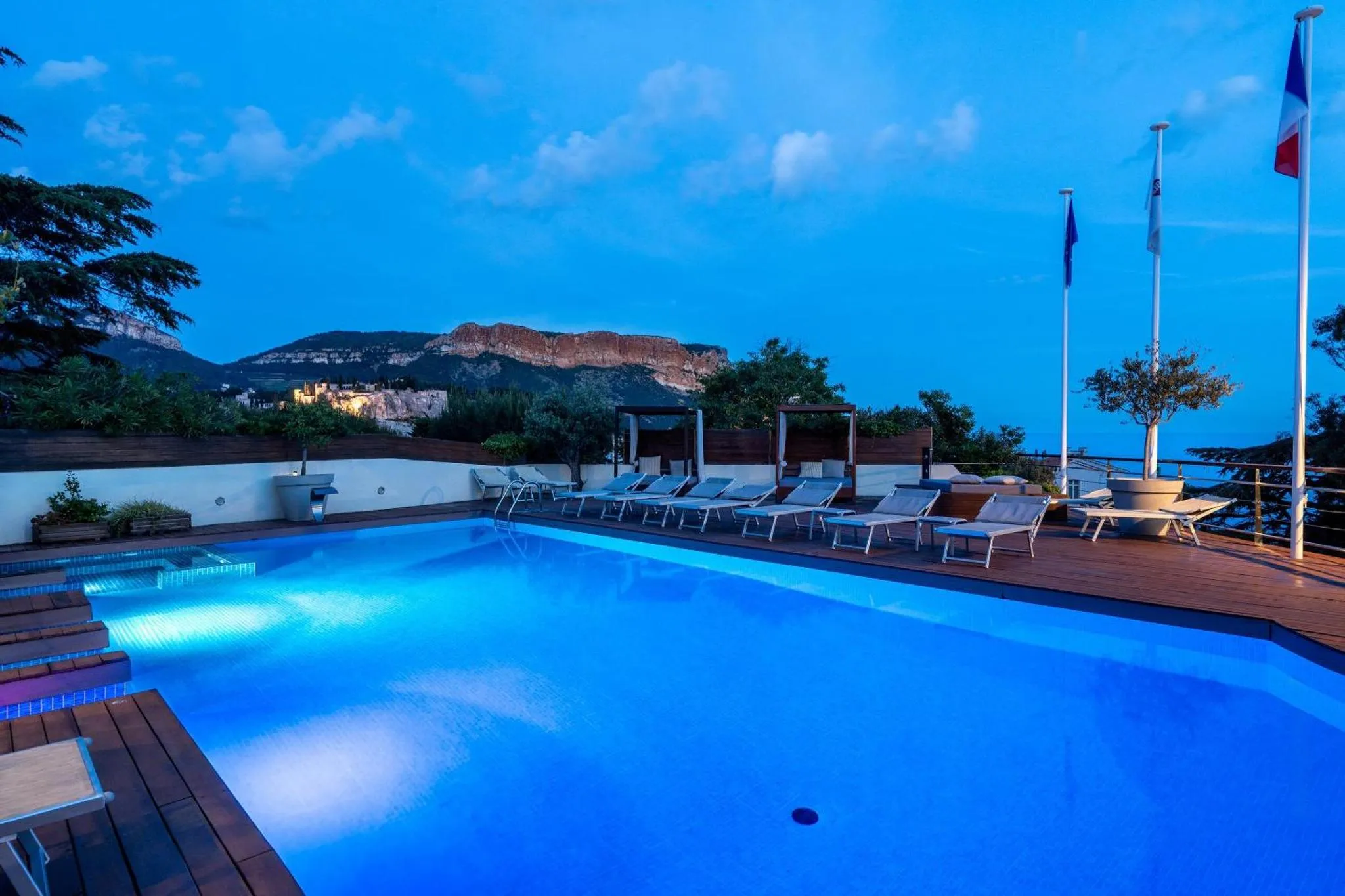 Terrasse avec piscine illuminée et vue sur la mer au crépuscule.