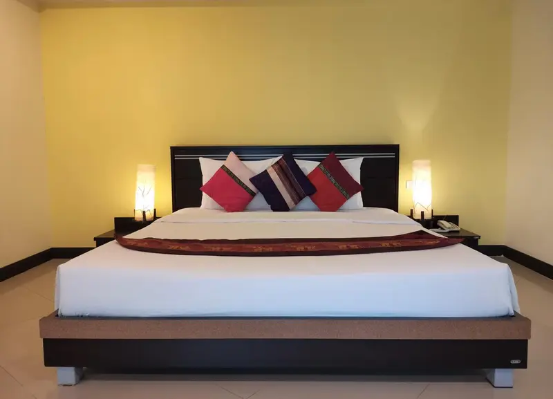 Un grand lit recouvert de coussins est dispose dans une chambre aux murs jaunes.