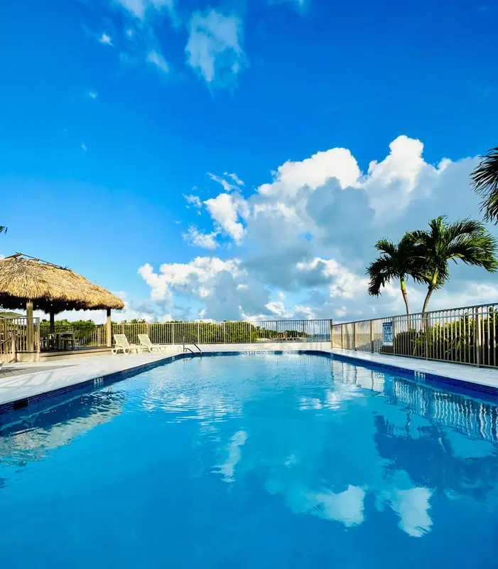 Une piscine rectangulaire bleu clair reflète le ciel nuageux.