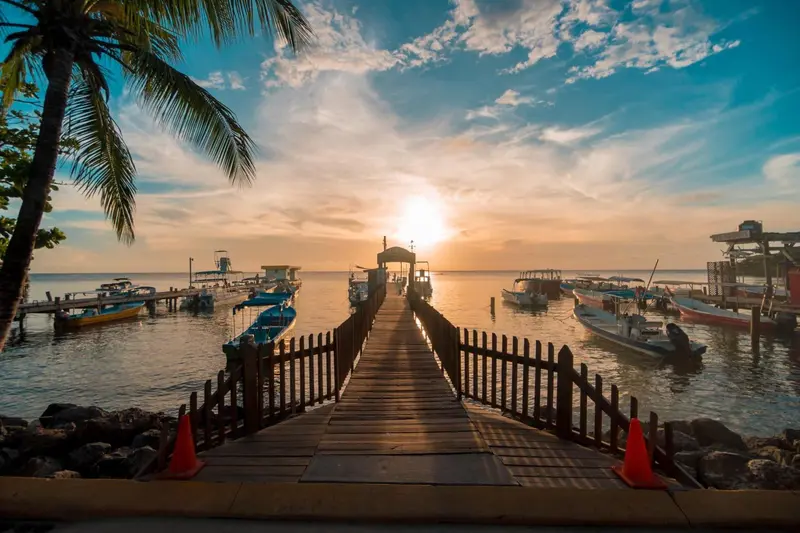 Un ponton en bois mène vers la mer au coucher du soleil.