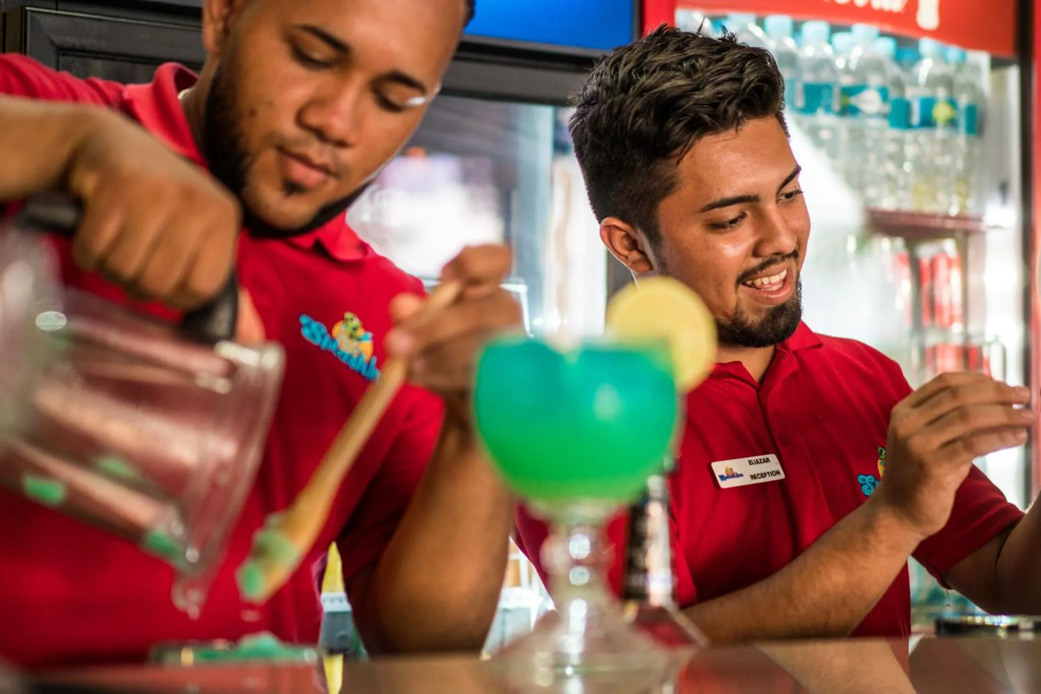 Deux hommes préparent des boissons colorées derrière un comptoir.