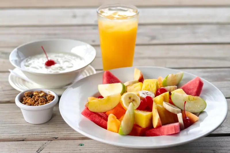Assiette de fruits frais et yaourt à la cerise sur une table en bois.