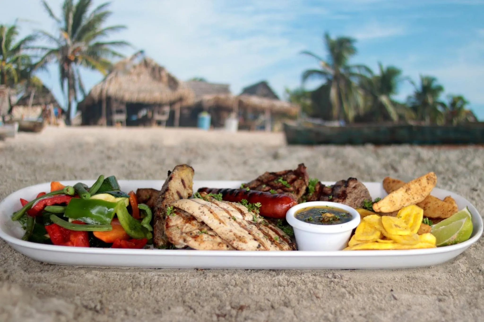 Assiette généreuse de grillades et de légumes frais présentée sur une plage de sable blanc.