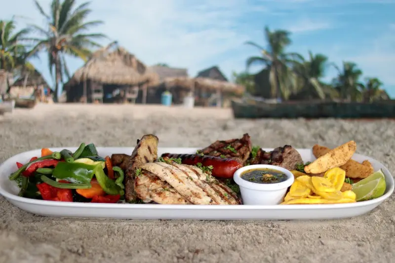 Assiette généreuse de grillades et de légumes frais présentée sur une plage de sable blanc.