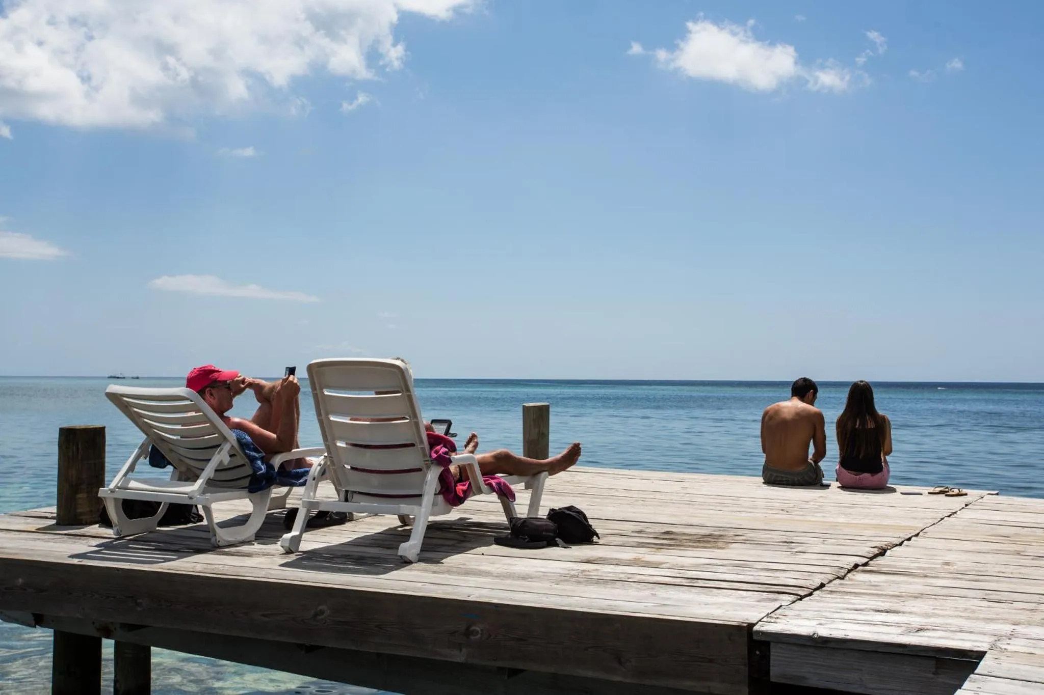 Deux personnes se détendent sur des transats en bois face à la mer.