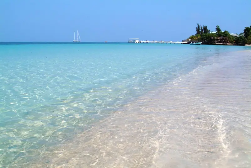 Plage de sable blanc bordée d'une eau turquoise et d'une végétation luxuriante.