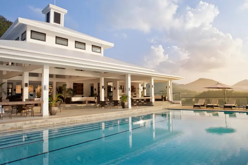 Une piscine turquoise reflète un bâtiment blanc avec une terrasse et des transats.