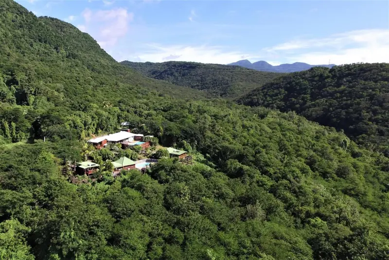 Vue aérienne d'un ensemble de bâtiments entourés d'une végétation luxuriante et de collines verdoyantes.