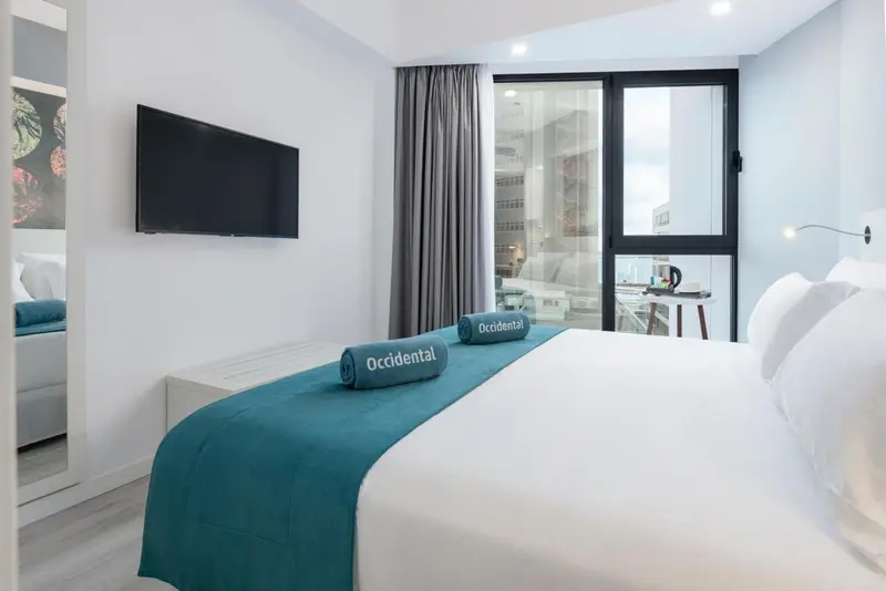 Une chambre lumineuse avec un grand lit et une télévision murale.