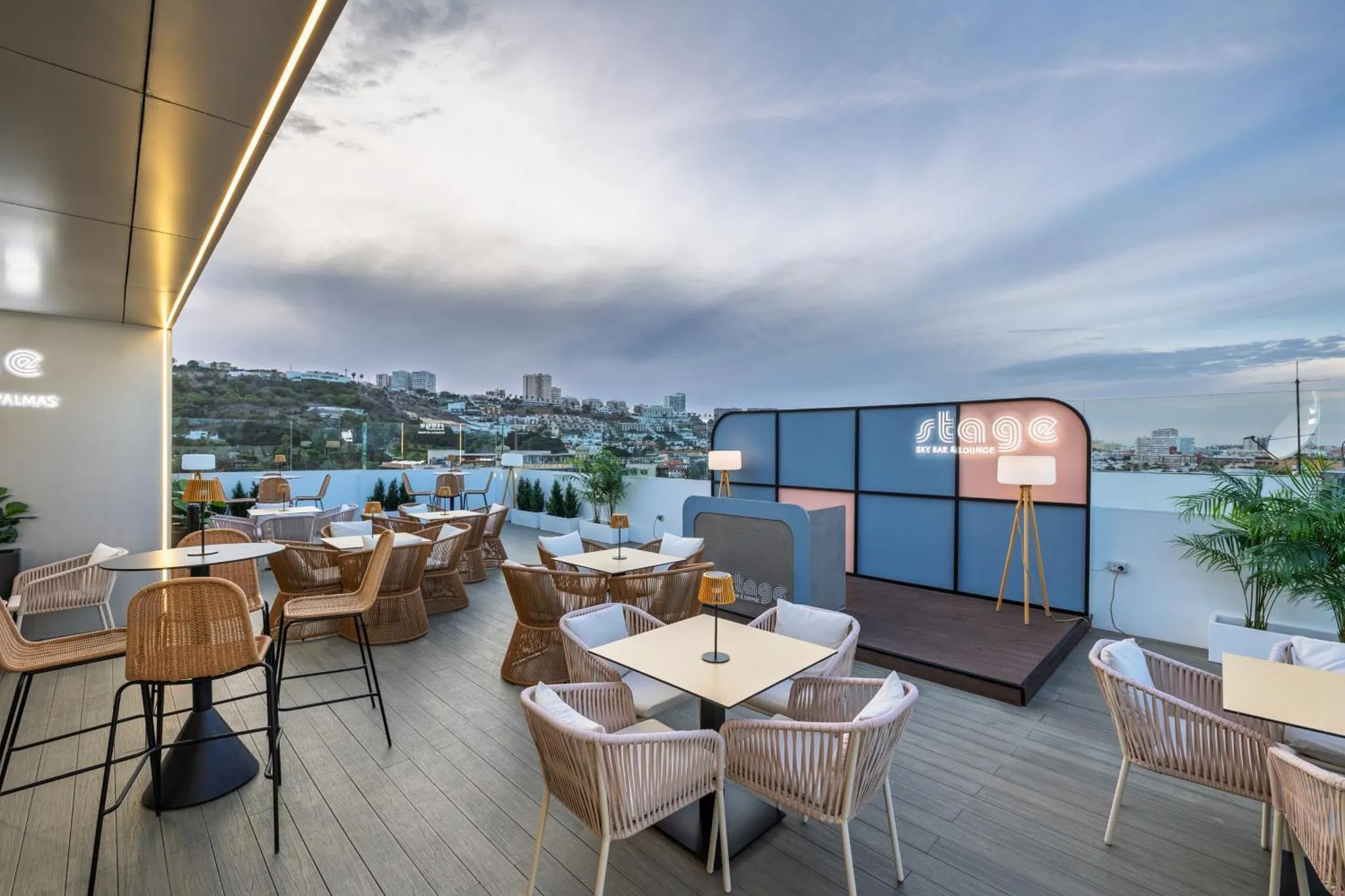 Terrasse aménagée avec tables, chaises et scène musicale, offrant une vue sur la ville.