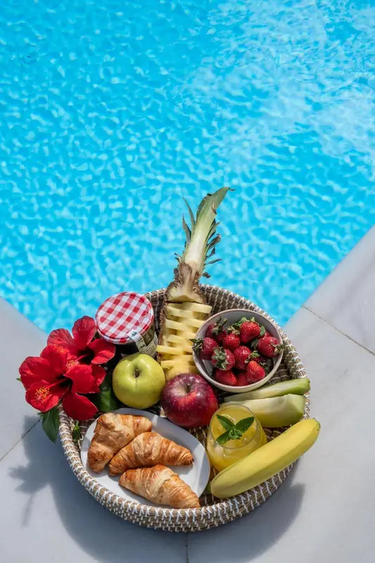Un panier de fruits frais et de viennoiseries est posé au bord d'une piscine.