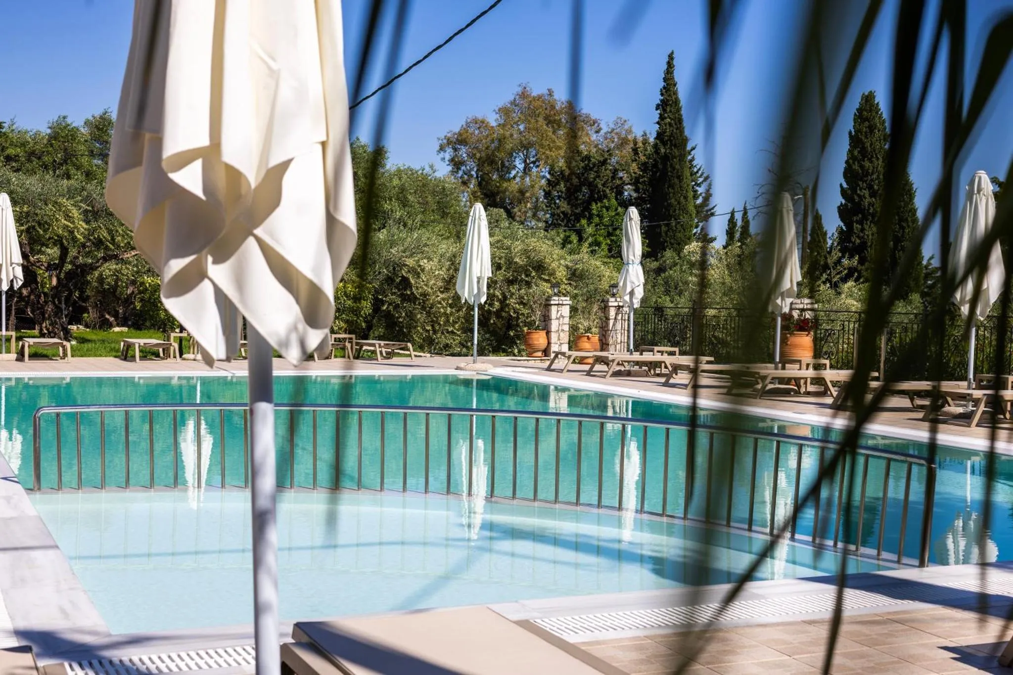 Une piscine turquoise bordée de transats et d'ombrelles blanches, entourée de végétation luxuriante.