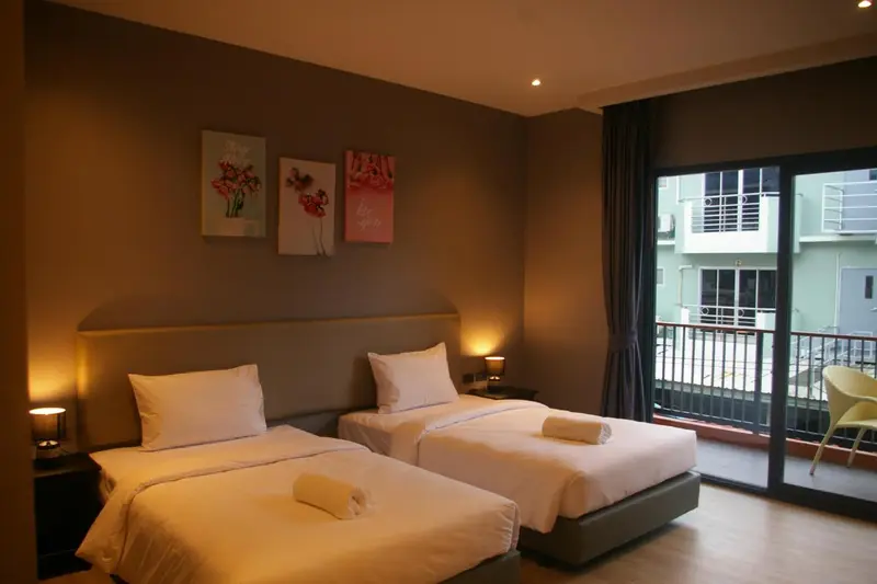 Chambre lumineuse avec deux lits simples et accès à un balcon.