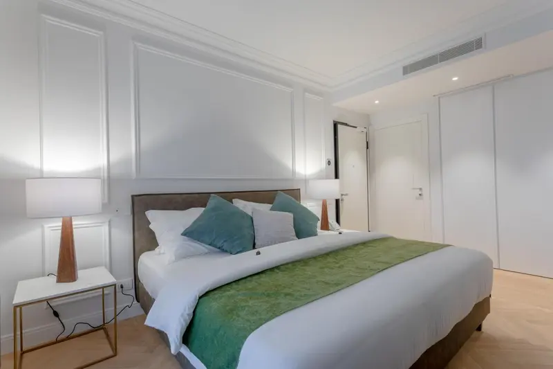 Une chambre lumineuse avec un grand lit recouvert d'une courtepointe verte et de coussins.