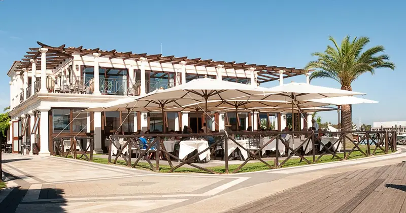Terrasse ombragée avec tables nappées en bord de mer.
