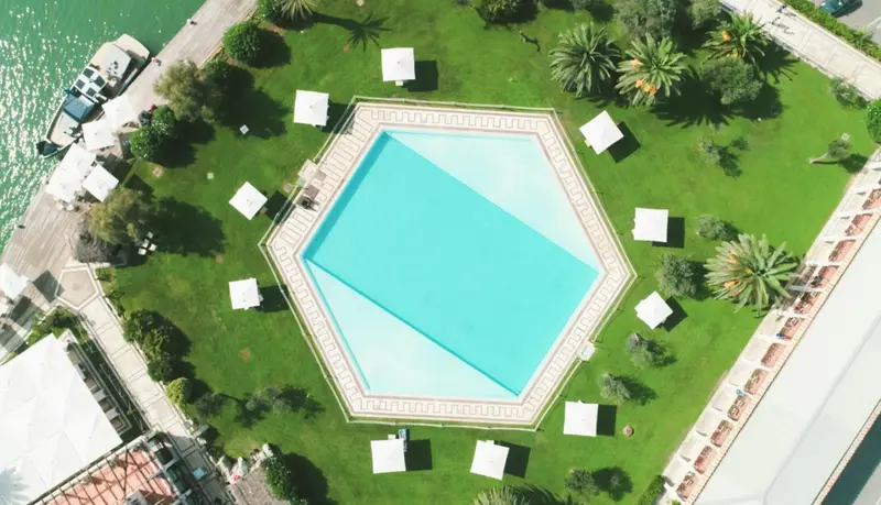 Vue aérienne d'une piscine hexagonale entourée d'une pelouse verdoyante et de palmiers.