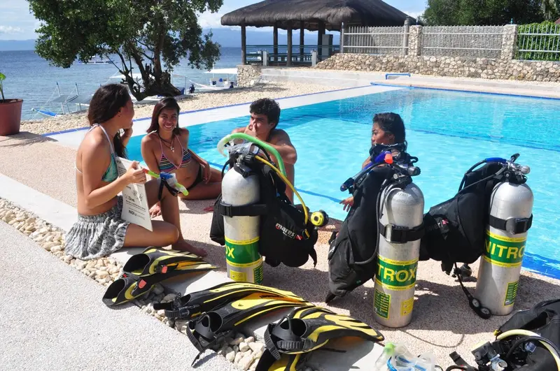 Des personnes discutent près d'une piscine avec des équipements de plongée à proximité.