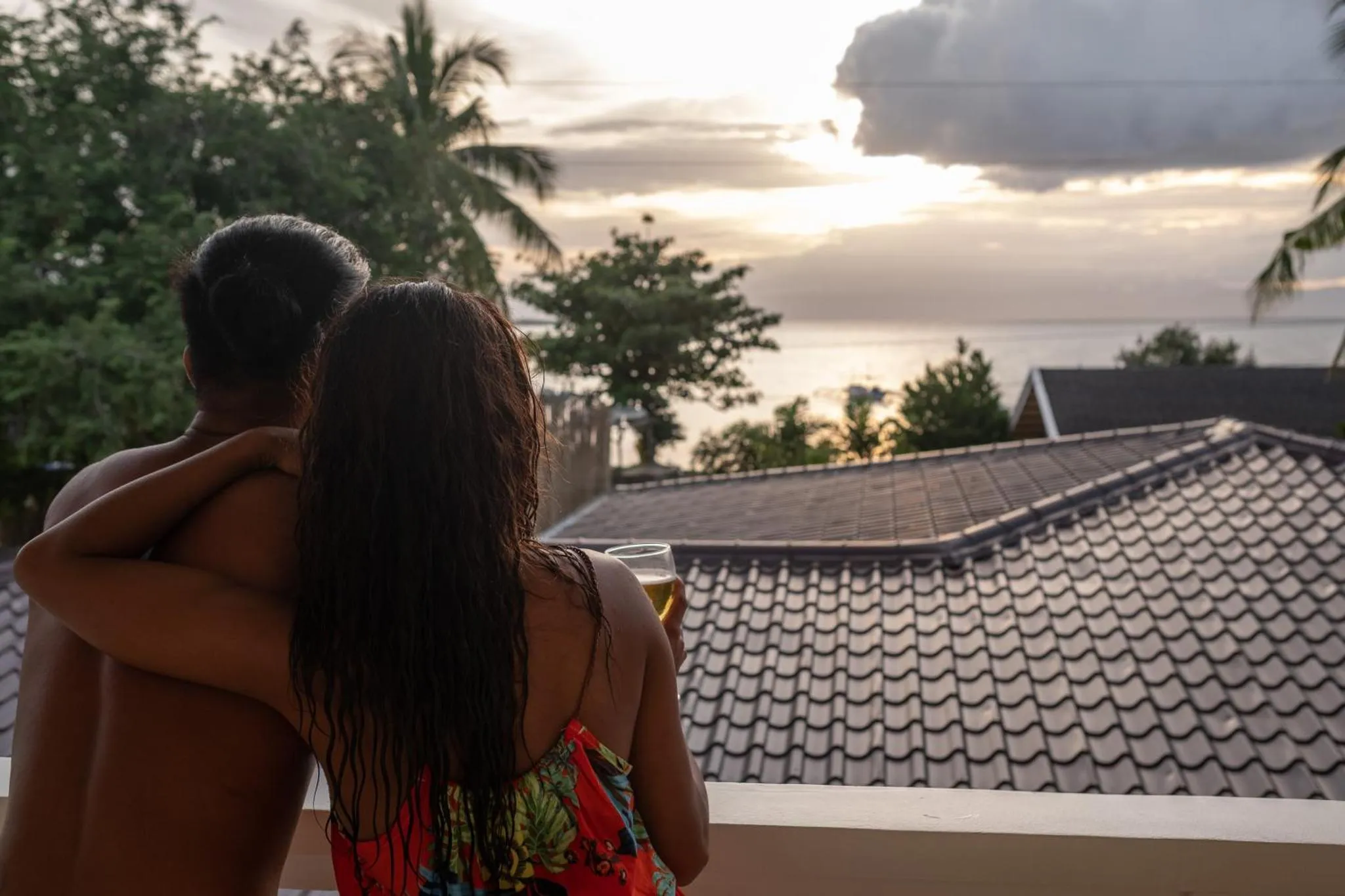 Un couple se tient sur une terrasse en admirant le coucher de soleil sur la mer.