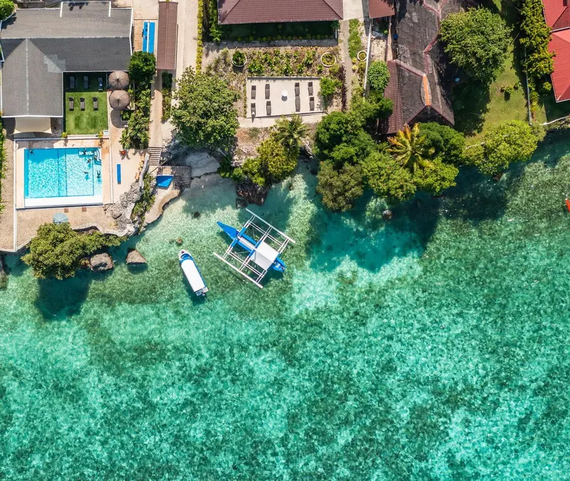 Vue aérienne d'un complexe hôtelier avec piscine et embarcations sur une eau turquoise.