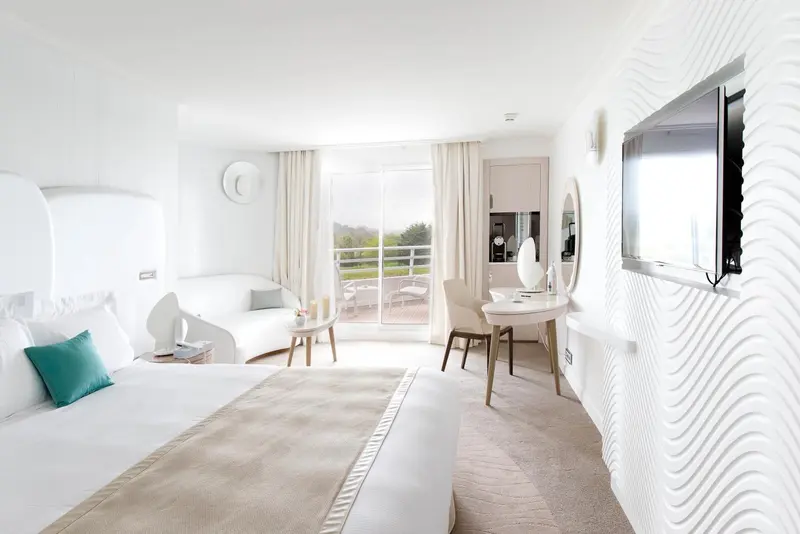 Chambre lumineuse avec un grand lit et un accès à une terrasse.