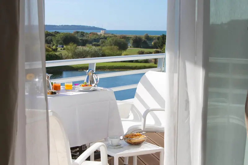 Une table de petit-déjeuner est dressée sur une terrasse ensoleillée avec vue sur la mer.