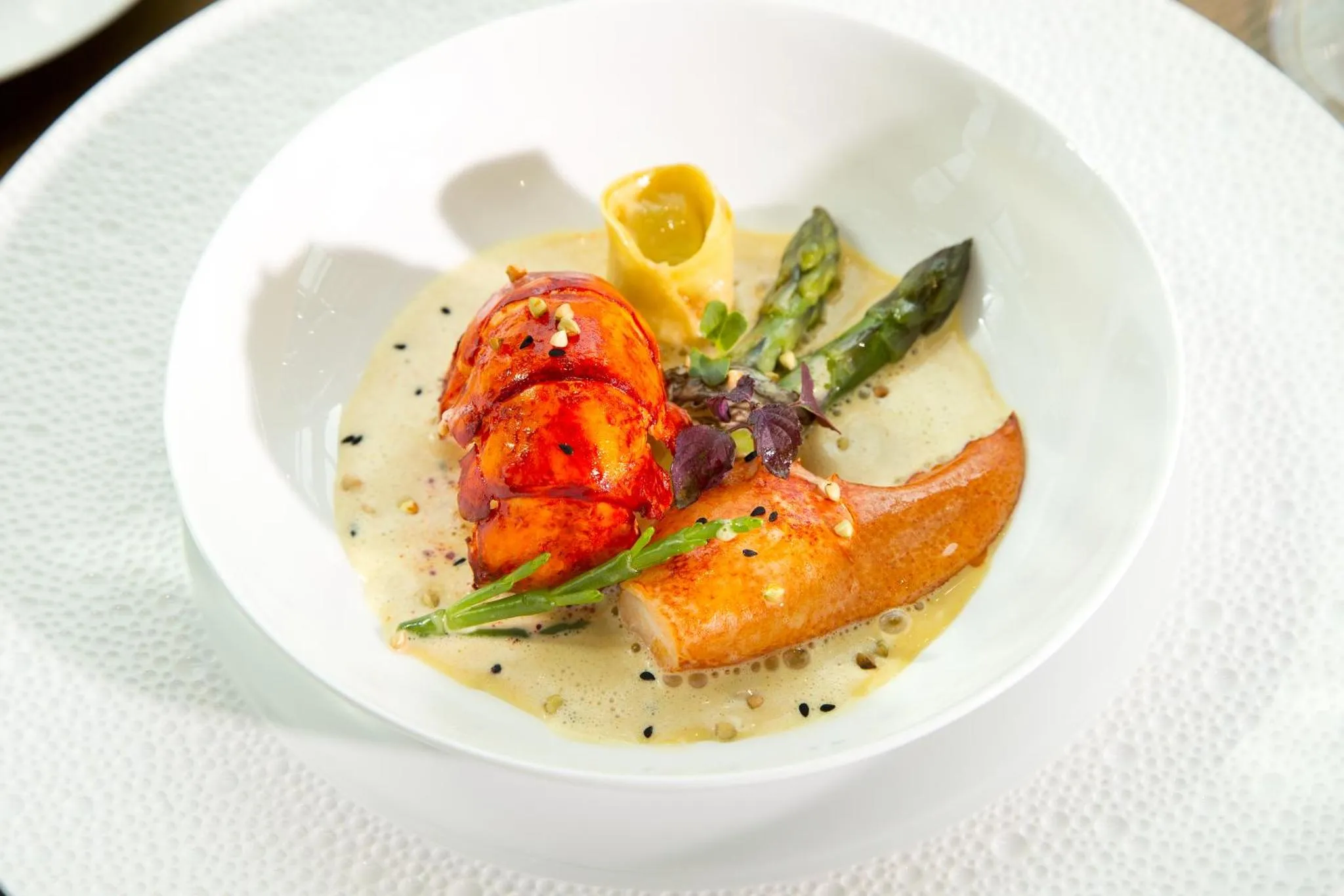 Présentation raffinée d'un plat de homard avec une sauce crémeuse et des légumes verts.