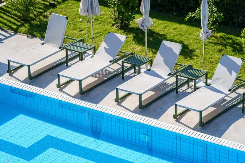 Transats blancs alignés au bord d'une piscine turquoise.